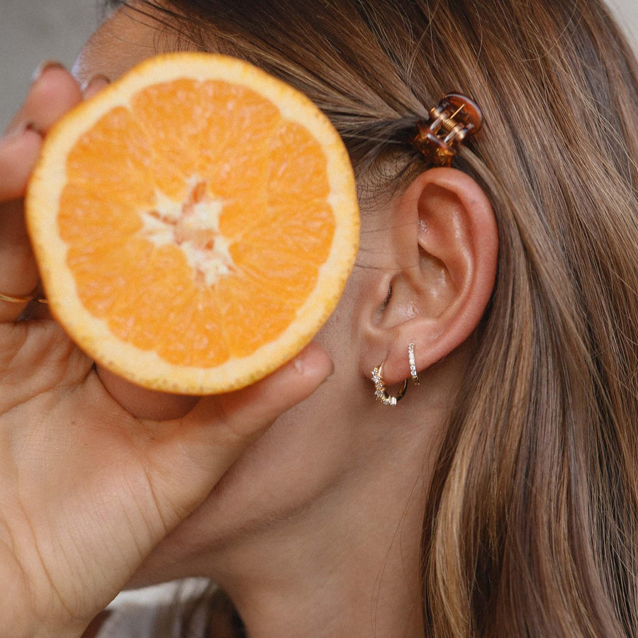 Woman holding an orange and wearing Gold Huggie Earrings - womens jewellery by Australian jewellery brands online indie and Harper 