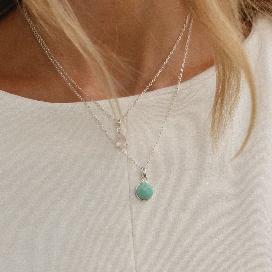 woman wearing two sterling silver necklaces, one with a rose quartz stone pendant and the other with a round turquoise stone pendant