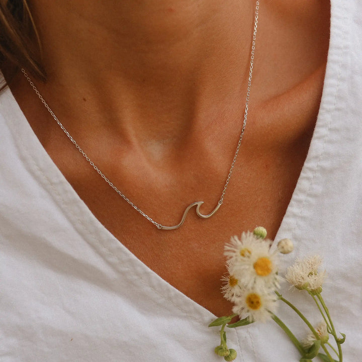 Woman in a white top holding flowers wearing a sterling silver wave necklace - womans sterling silver necklaces by Australian jewellery brands indie and harper