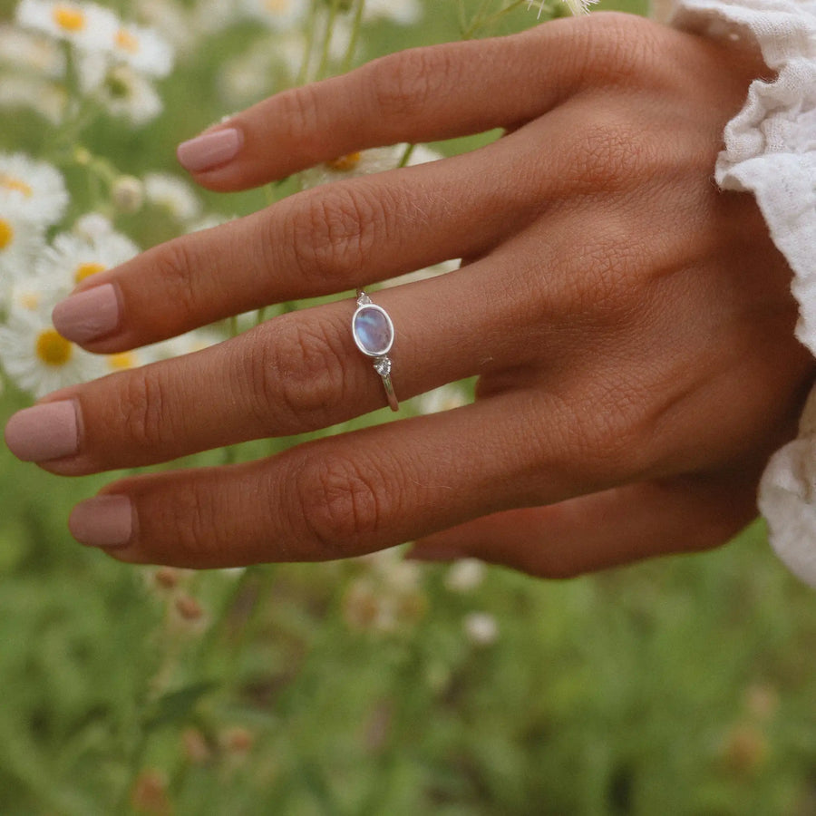 Woman's hand above a field of flowers, wearing a white topaz and moonstone ring - promise rings and moonstone jewellery by australian jewellery brands online indie and harper