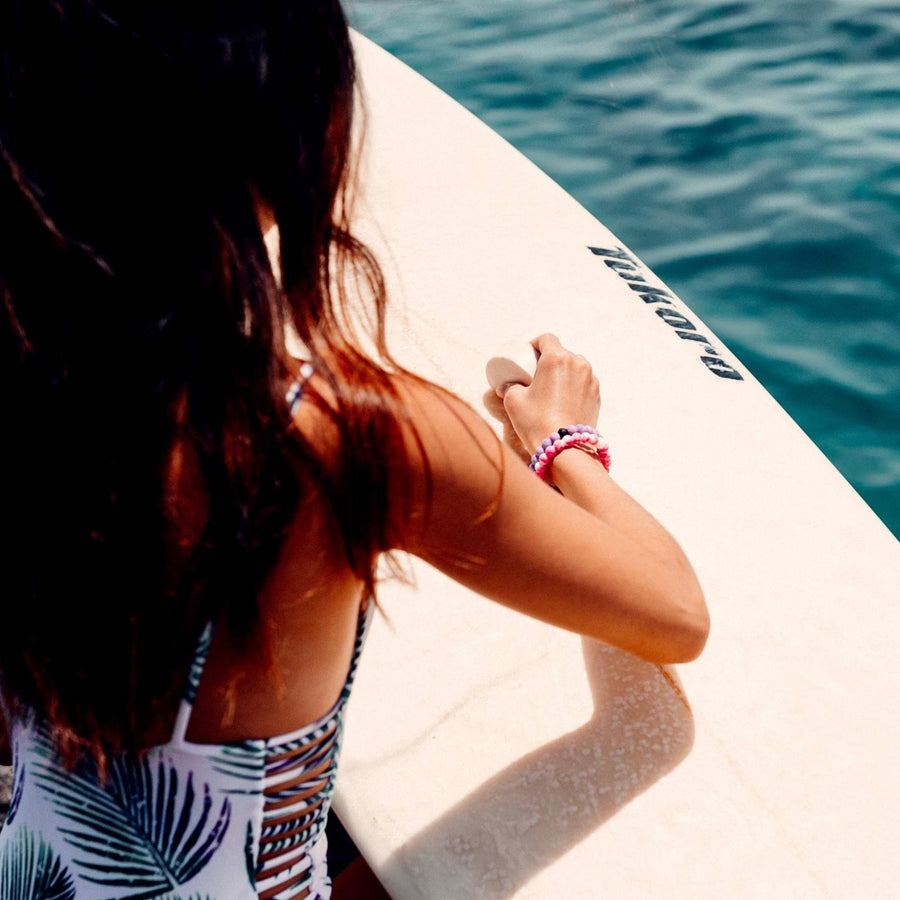 Woman standing with surf board wearing Lokai Bracelets - womens waterproof jewellery by Australian jewellery brands indie and harper