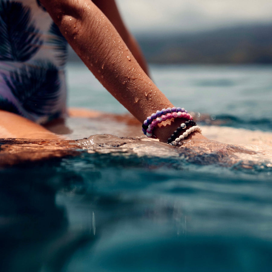 Person on surf board wearing Lokai Bracelets - waterproof jewellery by Australian jewellery brands indie and harper